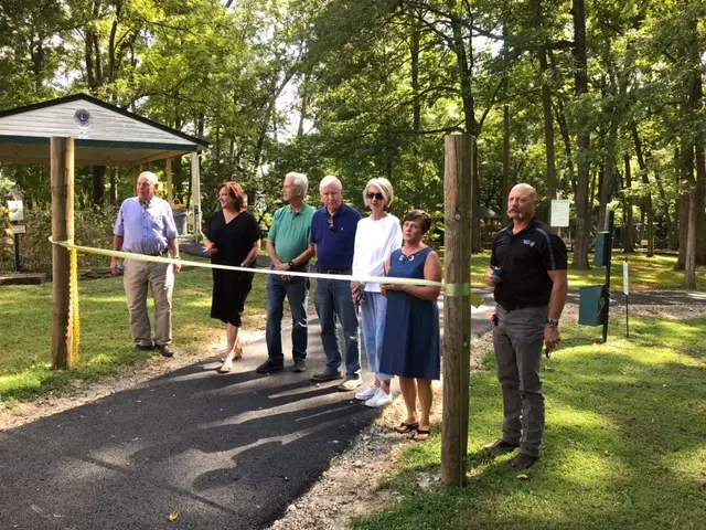 Group of town leaders standing behind ribbon stretched across paved trail in the park.