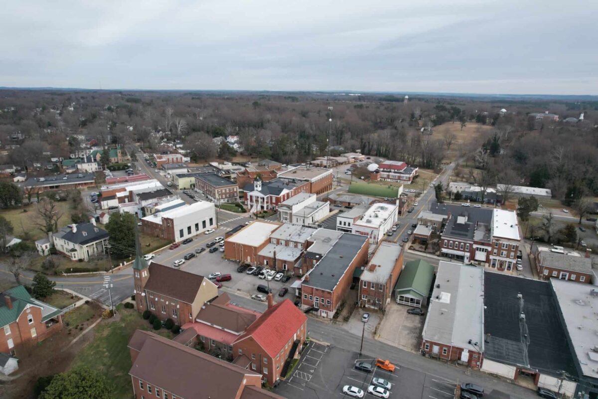 Aerial view of Chatham, looking toward the courthouse, showing downtown buildings and surrounding streets, set against a backdrop of trees and cloudy sky.