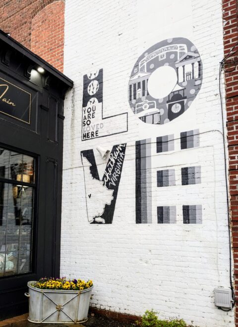 Mural on a brick wall spelling "LOVE" with "You Are So Loved Here" text.