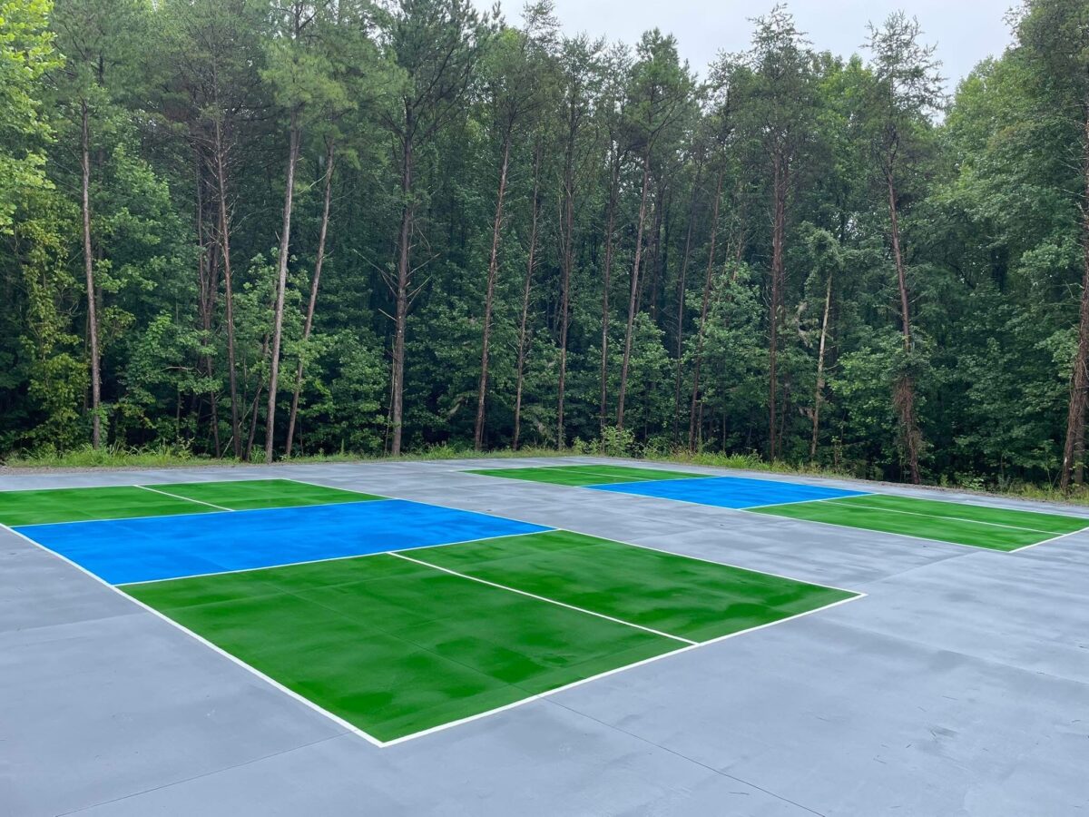 Two outdoor blue and green pickleball courts, surrounded by tall trees.